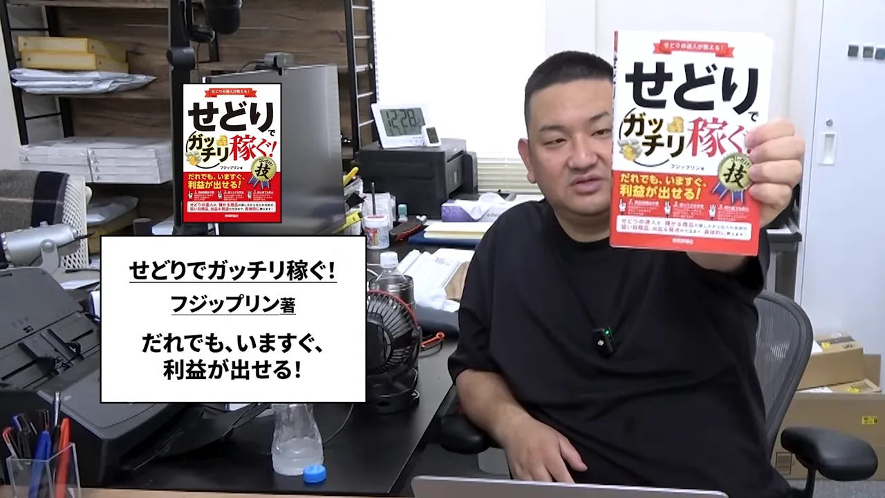 人物が書籍『せどりでガッチリ稼ぐ!』の表紙を手に持って見せているオフィス内の写真
