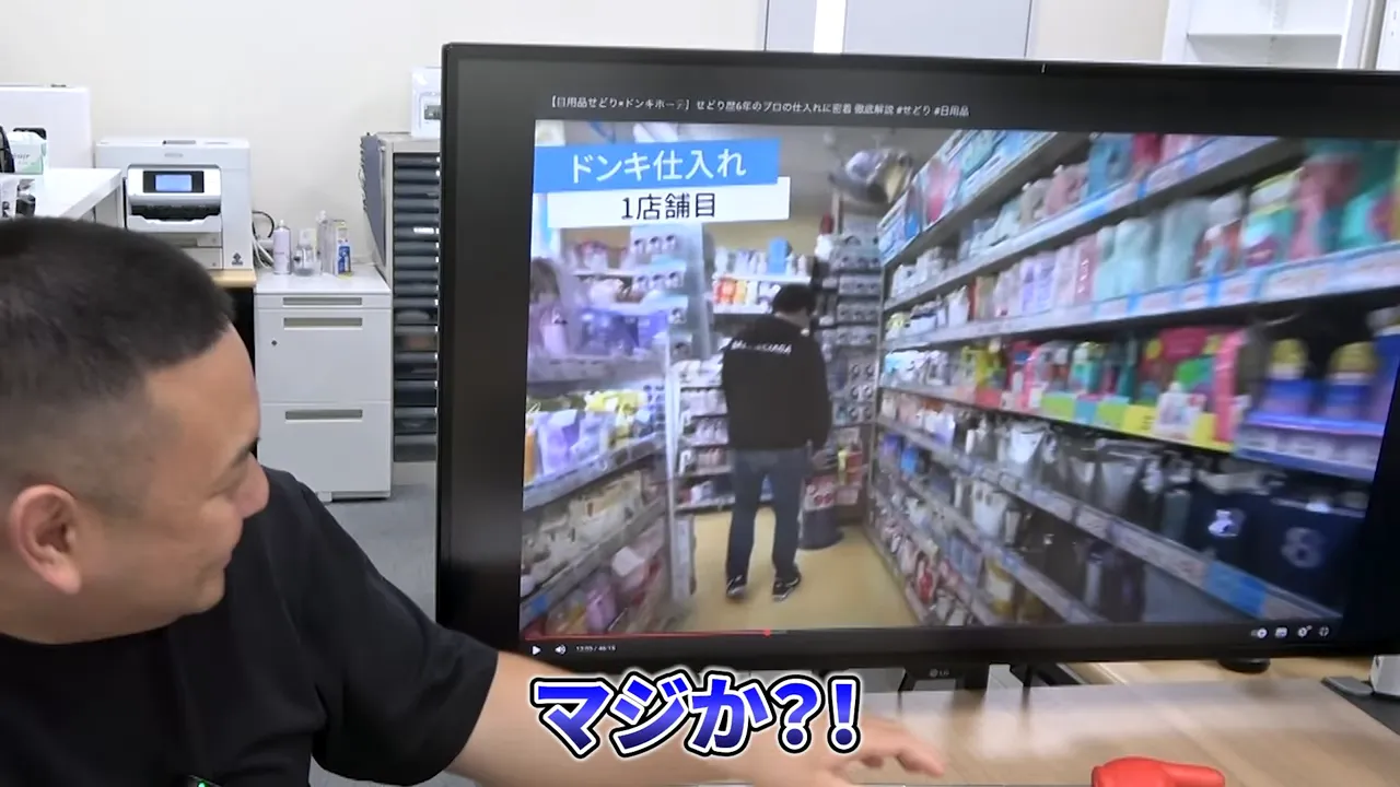 デスクのモニターに表示されたドン・キホーテの店舗内通路の広角映像。手前にデスクと人物が写る