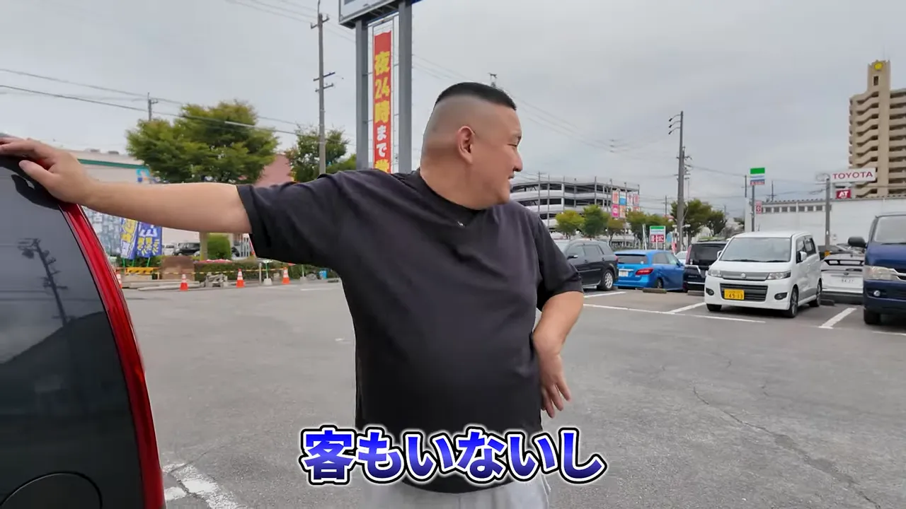 駐車場で周囲を見渡す男性。画面下に字幕「客もいないし」